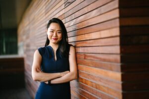 asian woman standing against wall smiling at camera