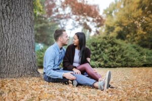 couple sitting on ground by a tree talking and smiling at each other