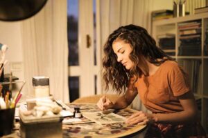 photo of a woman sitting at a desk smiling as she is working on a craft