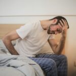 man sitting on bed with his head resting in his hands looking stressed and tired