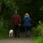 foto de una pareja paseando a su perro por una pista forestal