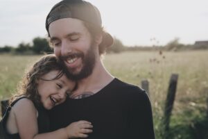 photo of a dadstanding in a field with his daughter smiling as she leans against his shoulder