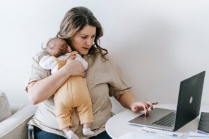 Young working mother cuddling baby and using laptop at home
