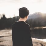man-standing-on-brown-soil-facing-body-of-water